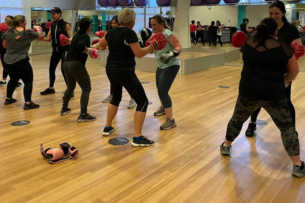 A full Boxing class working in pairs with red gloves on the timber studio floor