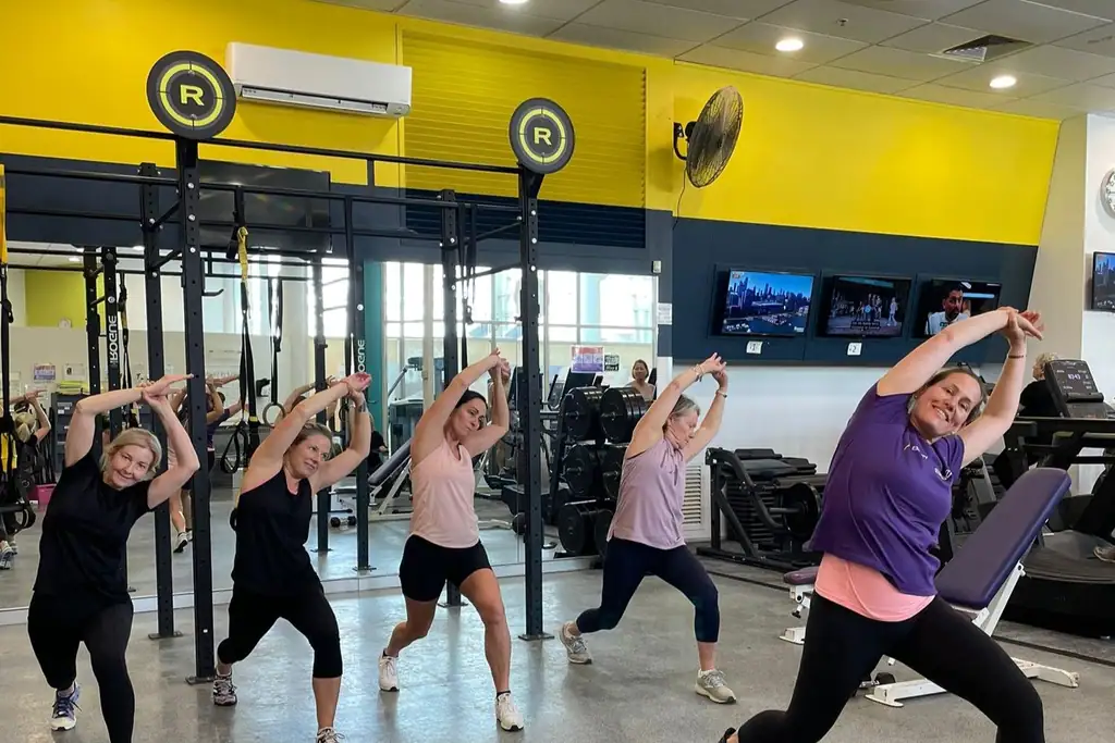 Members mid-exercise in a small group session in front of the yellow feature wall