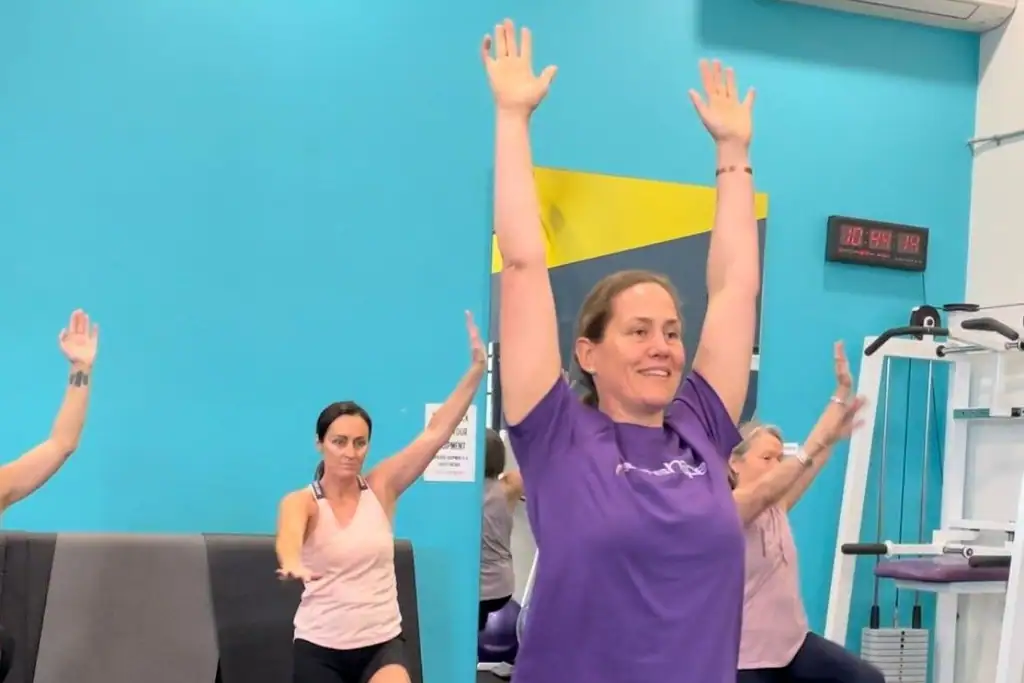 Members with arms raised at the end of a small group class by the teal wall