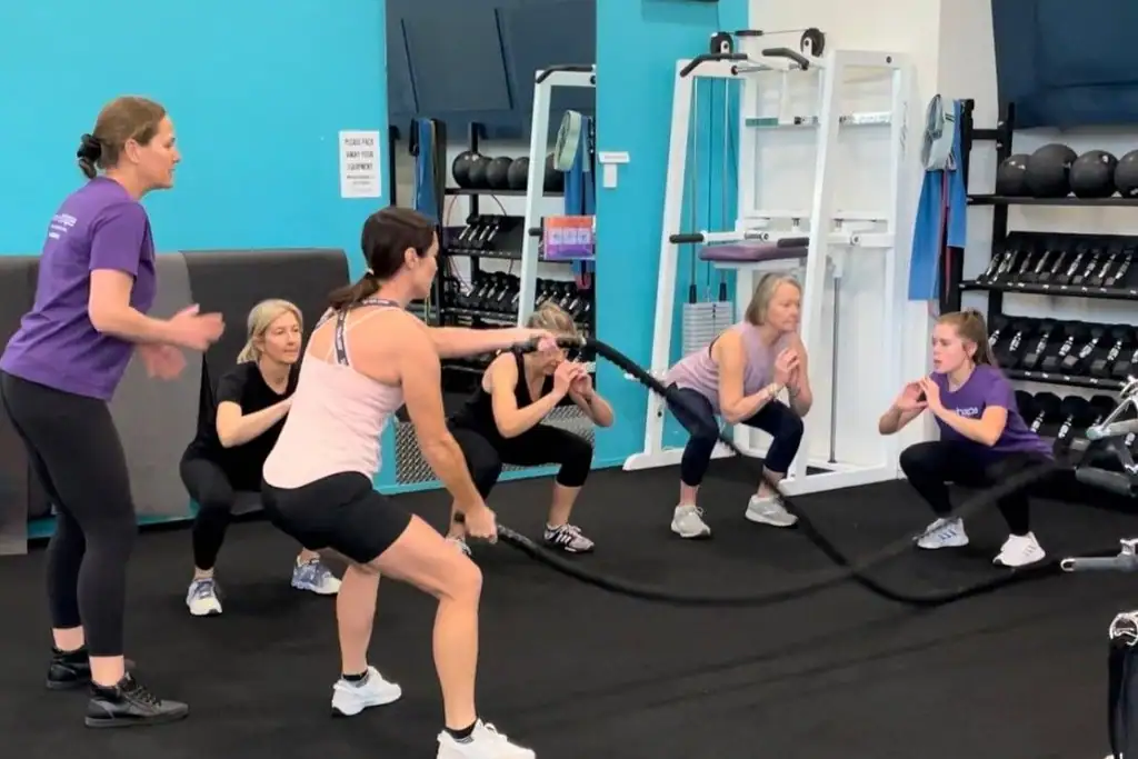 A member working battle ropes while the group trains behind her