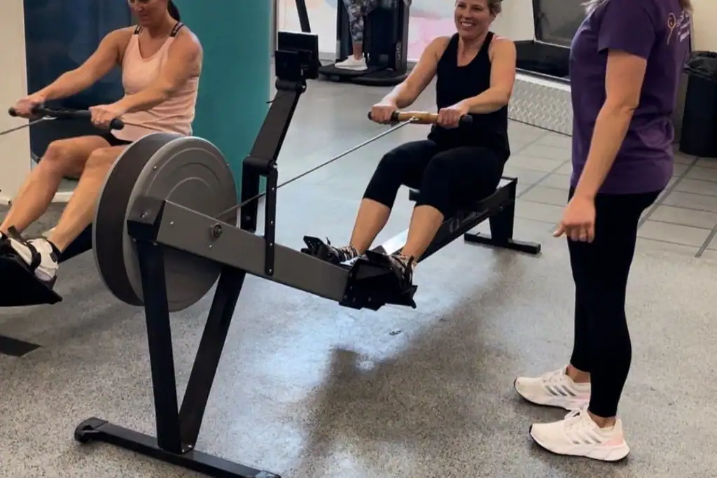 A trainer coaching two members through rowing intervals